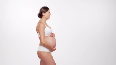 Genç, mutlu ve sağlıklı hamile bir kadın beyaz arka planda. Stüdyo videosu. Bebek beklentisi, hamilelik ve annelik kavramı.