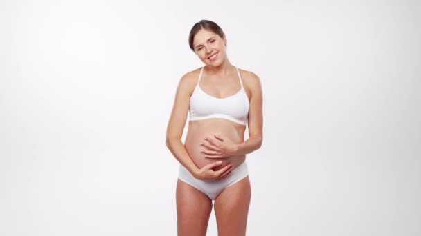 Mladá, šťastná a zdravá těhotná žena na bílém pozadí. Studio video. Dětské očekávání, těhotenství a mateřství koncept.
