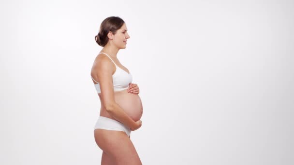 Mujer embarazada joven, feliz y saludable sobre fondo blanco. Vídeo del estudio. Esperanza del bebé, embarazo y concepto de maternidad. — Vídeos de Stock