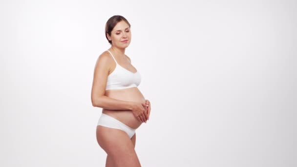 Jeune femme enceinte heureuse et en bonne santé sur fond blanc. Vidéo studio. Concept d'attente, de grossesse et de maternité du bébé. — Video