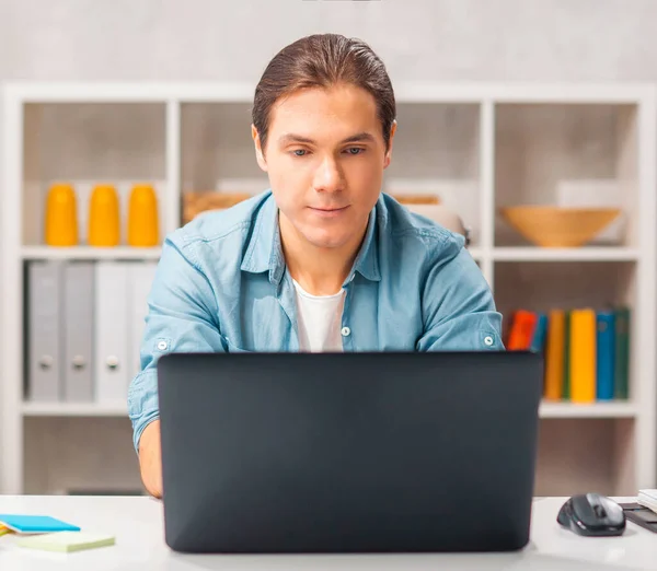 Un tânăr lucrează la un laptop. Freelancer, lucrător la distanță sau la locul de muncă al studenților. Conceptul de muncă la distanță. — Fotografie, imagine de stoc