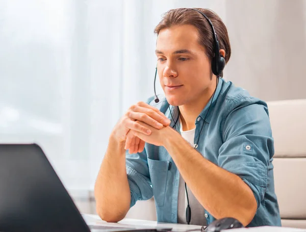 Un joven con auriculares trabaja en una computadora portátil. Freelancer, trabajador remoto o lugar de trabajo estudiantil. Concepto de trabajo distante. —  Fotos de Stock