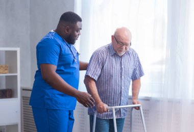 Bakıcı yaşlı adama Walker 'la yürümeyi öğretiyor. Bakımevindeki profesyonel hemşire ve hasta. Yardım, rehabilitasyon ve sağlık.