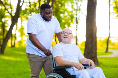 Caregiver and old man in a wheelchair. Professional nurse and patient walking outdoor in the park at sunset. Assistance, rehabilitation and health care. clipart