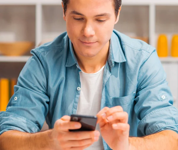 Giovane con uno smartphone si siede a tavola a casa. Libero professionista, lavoratore a distanza o studente sul posto di lavoro. Concetto di lavoro distante. — Foto Stock