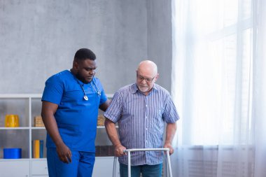 Bakıcı yaşlı adama Walker 'la yürümeyi öğretiyor. Bakımevindeki profesyonel hemşire ve hasta. Yardım, rehabilitasyon ve sağlık.