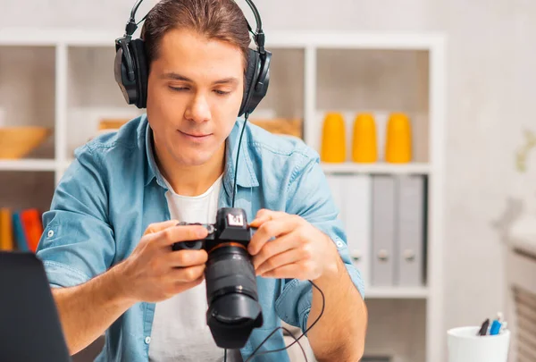 Freischaffende Fotografen am Arbeitsplatz. Ein junger Mann mit Kamera sitzt an einem Tisch und betrachtet Fotos. Fernarbeits-Konzept. — Stockfoto