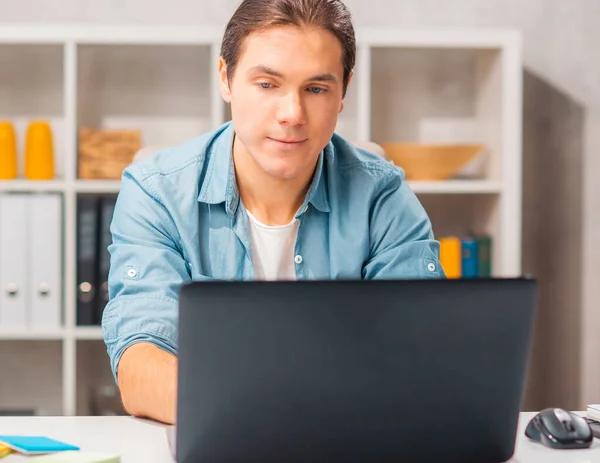 Un tânăr lucrează la un laptop. Freelancer, lucrător la distanță sau la locul de muncă al studenților. Conceptul de muncă la distanță. — Fotografie, imagine de stoc