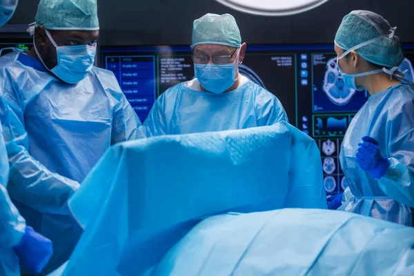 El equipo multirracial de cirujanos médicos profesionales realiza la operación quirúrgica en un hospital moderno. Los médicos están trabajando para salvar al paciente. Medicina, salud y neurocirugía. —  Fotos de Stock