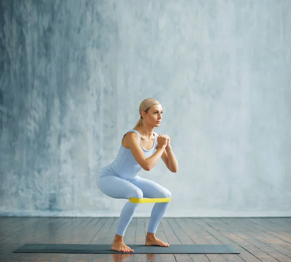 Jonge slanke blonde vrouw in sportkleding houdt zich bezig met fitness in een ruime trainingsruimte. Sport, gezondheid, gymnastiek en leefstijl. — Stockfoto