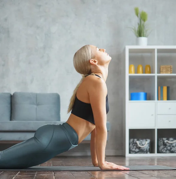 Mulher loira esbelta jovem em sportswear envolve-se na aptidão em casa. Conceito de desporto, saúde e estilo de vida. — Fotografia de Stock