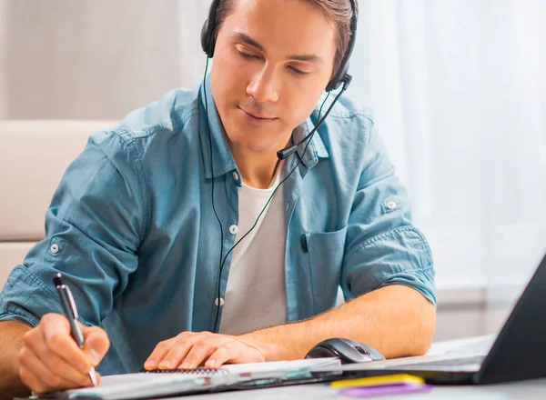 Egy fiatal férfi egy fejhallgatóban egy laptopnál dolgozik. Szabadúszó, távmunkás vagy diákmunkahely. Távoli munkavégzés fogalma. — Stock Fotó