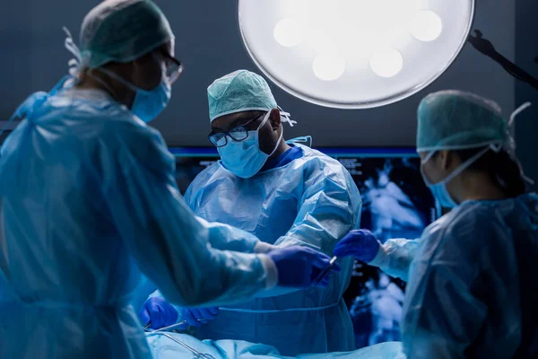 Multiracial team of professional medical surgeons performs the surgical operation in a modern hospital. Doctors are working to save the patient. Medicine, health, cardiology and transplantation. — Stock Photo, Image