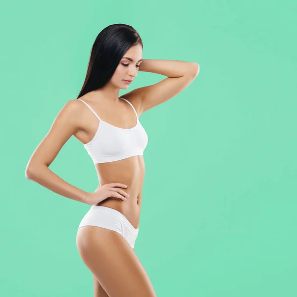 Jonge, fitte en mooie brunette vrouw in wit badpak poserend in de studio. Concept van fitness, dieet en huidverzorging. — Stockfoto
