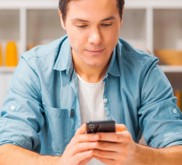 Ung man med en smartphone sitter vid bordet hemma. Frilansare, distansarbetare eller studentarbetsplats. Begreppet distansarbete. — Stockfoto