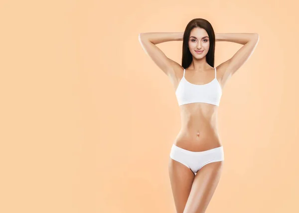Junge, fitte und schöne brünette Frau im weißen Badeanzug posiert im Studio. Konzept von Fitness, Diät und Hautpflege. — Stockfoto