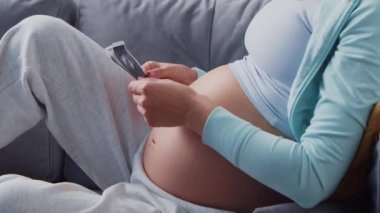 Genç hamile kadın evde dinleniyor ve bebek bekliyor. Hamilelik, annelik, sağlık ve yaşam tarzı kavramı.