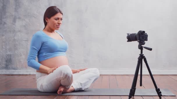 A young pregnant woman makes a vlog about yoga exercises and meditation. The influencer records videos or streams on a camera. — Stock Video