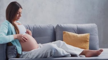 Genç hamile kadın evde dinleniyor ve bebek bekliyor. Hamilelik, annelik, sağlık ve yaşam tarzı kavramı.