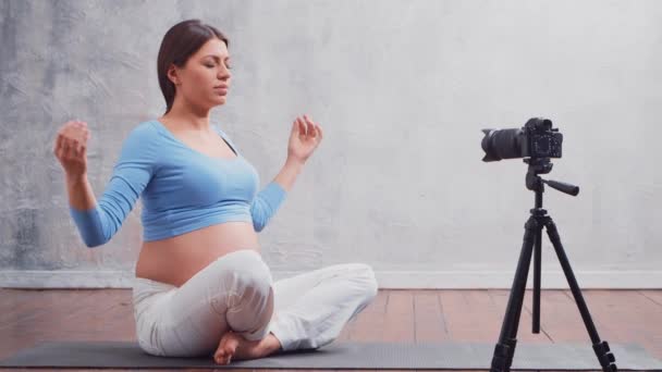 Genç hamile bir kadın yoga egzersizleri ve meditasyonla ilgili bir video bloğu hazırlıyor. Etkilenen kişi bir kameraya video veya akış kaydeder. — Stok video