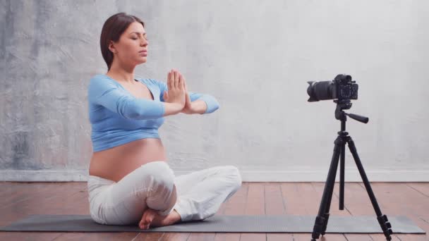 Una joven embarazada hace un vlog sobre ejercicios de yoga y meditación. El influencer graba videos o transmisiones en una cámara. — Vídeos de Stock