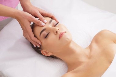 Güzel, genç ve sağlıklı bir kadın güzellik salonunda yüz masajı yaptırıyor. Profesyonel masörün elleri işte. Spa, sağlık ve iyileştirme kavramı.