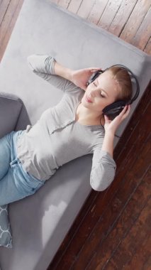 Genç ve güzel bir kız, kulaklıklarla kanepede uzanıp müzik dinliyor. Sarışın kadın evinde dinleniyor..