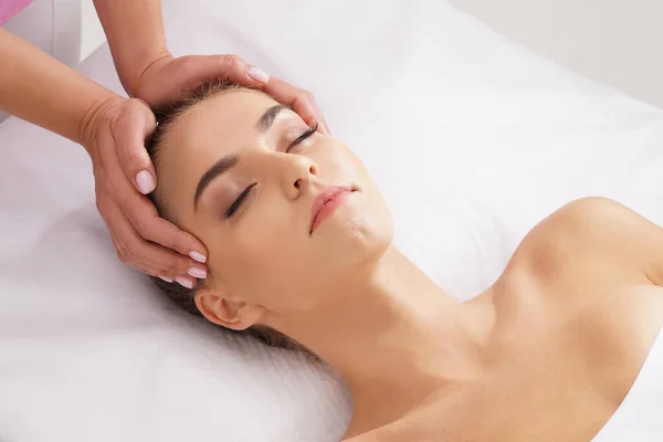 Schöne, junge und gesunde Frau mit Gesichtsmassage im Wellness-Salon. Hände eines professionellen Masseurs. Wellness-, Gesundheits- und Heilkonzept. — Stockfoto