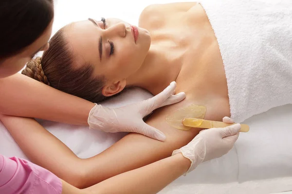 Beautician tar bort hår från unga kvinnliga armhålor med varmt vax. Kvinnan har en skönhetsbehandling. Depilering, epilering, hud- och hälsovårdsbegrepp. — Stockfoto