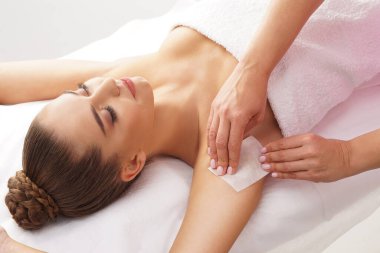 Güzellik uzmanı, genç kadın koltukaltlarındaki kılları sıcak balmumuyla alıyor. Kadının güzel bir titreme prosedürü var. Defilasyon, epilasyon, cilt ve sağlık konseptleri.