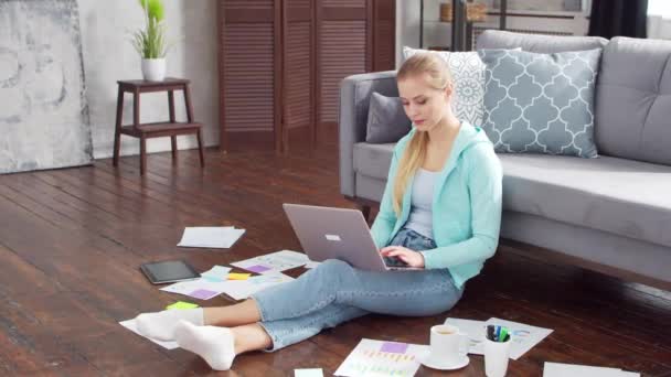 Молода жінка працює з документами, використовуючи ноутбук, сидячи на підлозі вдома. Студент, підприємець або дівчина-фрілансер, яка працює або навчається дистанційно. Концепція дистанційного навчання та роботи . — стокове відео