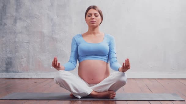 Mujer embarazada joven haciendo ejercicios de yoga y meditando en casa. El concepto de salud, mindfulness, relajación y bienestar. — Vídeo de stock