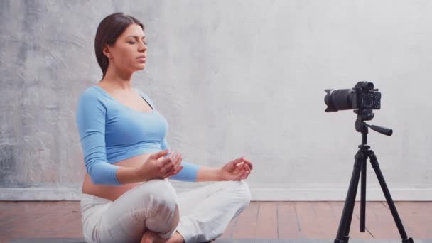 Una joven embarazada hace un vlog sobre ejercicios de yoga y meditación. El influencer graba videos o transmisiones en una cámara. — Vídeos de Stock