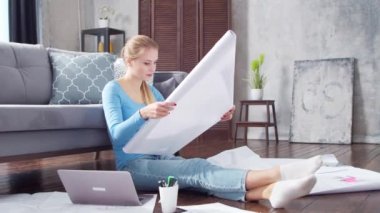 Genç bir kadın evde yerde otururken dizüstü bilgisayar kullanarak belgelerle çalışıyor. Öğrenci, girişimci ya da serbest çalışan ya da uzaktan eğitim gören bir kız. Mesafe öğrenme ve iş kavramı.