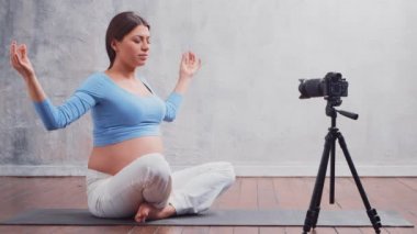 Genç hamile bir kadın yoga egzersizleri ve meditasyonla ilgili bir video bloğu hazırlıyor. Etkilenen kişi bir kameraya video veya akış kaydeder.