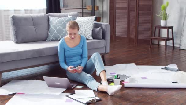 Женщина работает с документами, используя смартфон и ноутбук, сидя дома на полу. Студентка, предприниматель или девушка-фрилансер, работающая или обучающаяся дистанционно. Дистанционное обучение и концепция работы. — стоковое видео