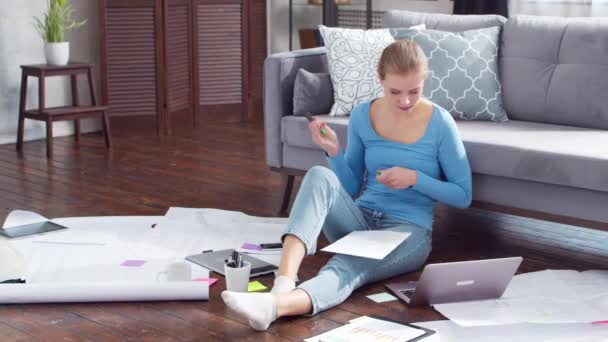 Mujer joven trabaja con documentos utilizando un ordenador portátil mientras está sentado en el suelo en casa. Estudiante, empresaria o freelancer que trabaja o estudia a distancia. Concepto de aprendizaje a distancia y empleo. — Vídeos de Stock