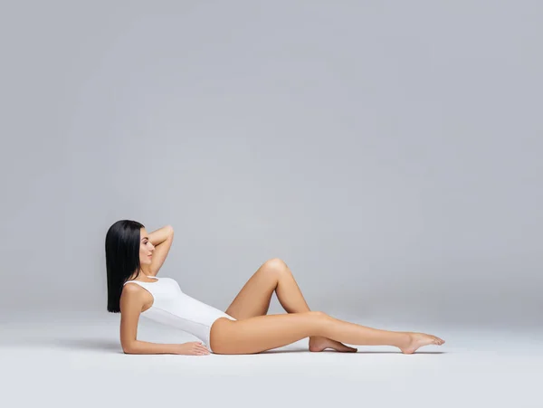 Jeune, en forme et belle femme brune en maillot de bain blanc posant en studio. Concept de fitness, régime et soins de la peau. — Photo