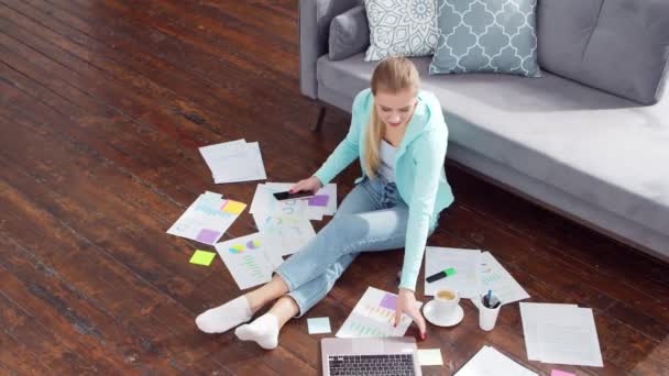 Ung kvinna arbetar med dokument med hjälp av en bärbar dator när du sitter på golvet hemma. Studerande, företagare eller frilansande flicka som arbetar eller studerar på distans. Begreppet distansutbildning och distansarbete. — Stockvideo