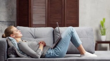 Genç bir kadın kanepede dizüstü bilgisayar kullanarak çalışıyor. Öğrenci, girişimci ya da serbest çalışan kız internet üzerinden çalışıyor ya da uzaktan öğrenim görüyor. Mesafe öğrenme ve iş kavramı.