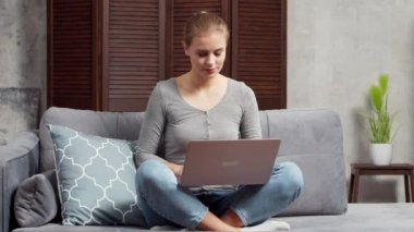 Genç kadın kanepede otururken dizüstü bilgisayar kullanıyor. Öğrenci, girişimci ya da serbest çalışan kız internet üzerinden çalışıyor ya da uzaktan öğrenim görüyor. Mesafe öğrenme ve iş kavramı.