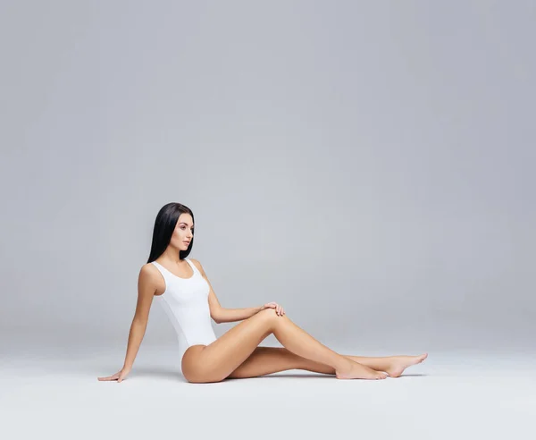 Attraktives und schlankes brünettes Mädchen in weißer Unterwäsche, das im Studio posiert. Gesunder Lebensstil, Sport und Körperpflege. — Stockfoto