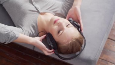 Genç ve güzel bir kız, kulaklıklarla kanepede uzanıp müzik dinliyor. Sarışın kadın evinde dinleniyor..
