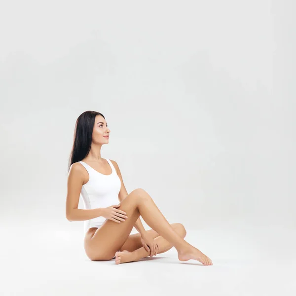 Junge, fitte und schöne brünette Frau im weißen Badeanzug posiert im Studio. Konzept von Fitness, Diät und Hautpflege. — Stockfoto