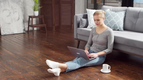 若い女性は自宅の床に座っている間、ノートパソコンを使用して文書で動作します。学生、起業家やフリーランスの女の子がリモートで働くか勉強します。距離学習と仕事の概念. — ストック動画