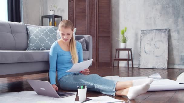 Mujer joven trabaja con documentos utilizando un ordenador portátil mientras está sentado en el suelo en casa. Estudiante, empresaria o freelancer que trabaja o estudia a distancia. Concepto de aprendizaje a distancia y empleo. — Vídeo de stock