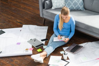 Genç bir kadın evde yerde otururken dizüstü bilgisayar kullanarak belgelerle çalışıyor. Öğrenci, girişimci veya serbest çalışan kız İnternet üzerinden çalışıyor veya uzaktan öğrenim görüyor.