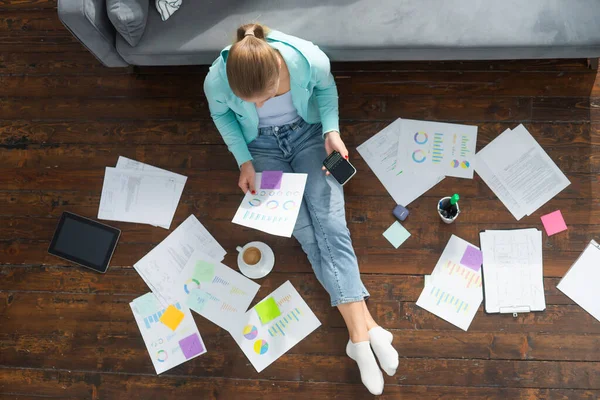 Junge Frau arbeitet mit Dokumenten, während sie zu Hause auf dem Fußboden sitzt. Studentin, Unternehmerin oder Freiberuflerin, die aus der Ferne über das Internet arbeitet oder studiert. — Stockfoto