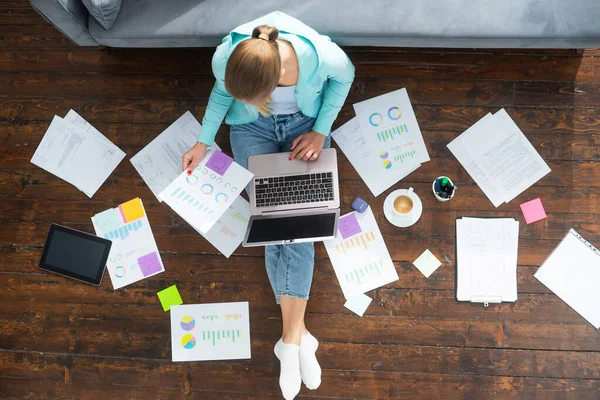 Junge Frau arbeitet mit Laptop mit Dokumenten, während sie zu Hause auf dem Boden sitzt. Studentin, Unternehmerin oder Freiberuflerin, die aus der Ferne über das Internet arbeitet oder studiert. — Stockfoto