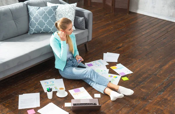 Junge Frau arbeitet mit Smartphone und Laptop mit Dokumenten, während sie zu Hause auf dem Boden sitzt. Studentin, Unternehmerin oder Freiberuflerin, die aus der Ferne über das Internet arbeitet oder studiert. — Stockfoto